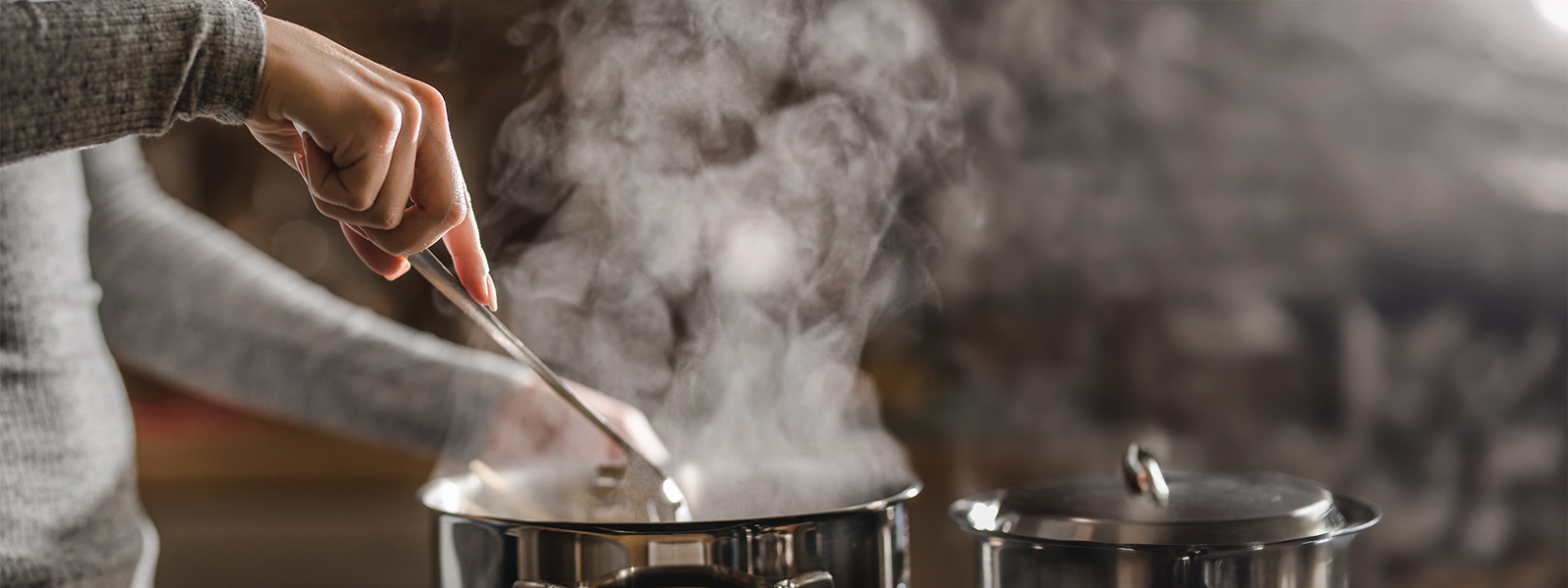 Steam rising out of a pot while a person cooks