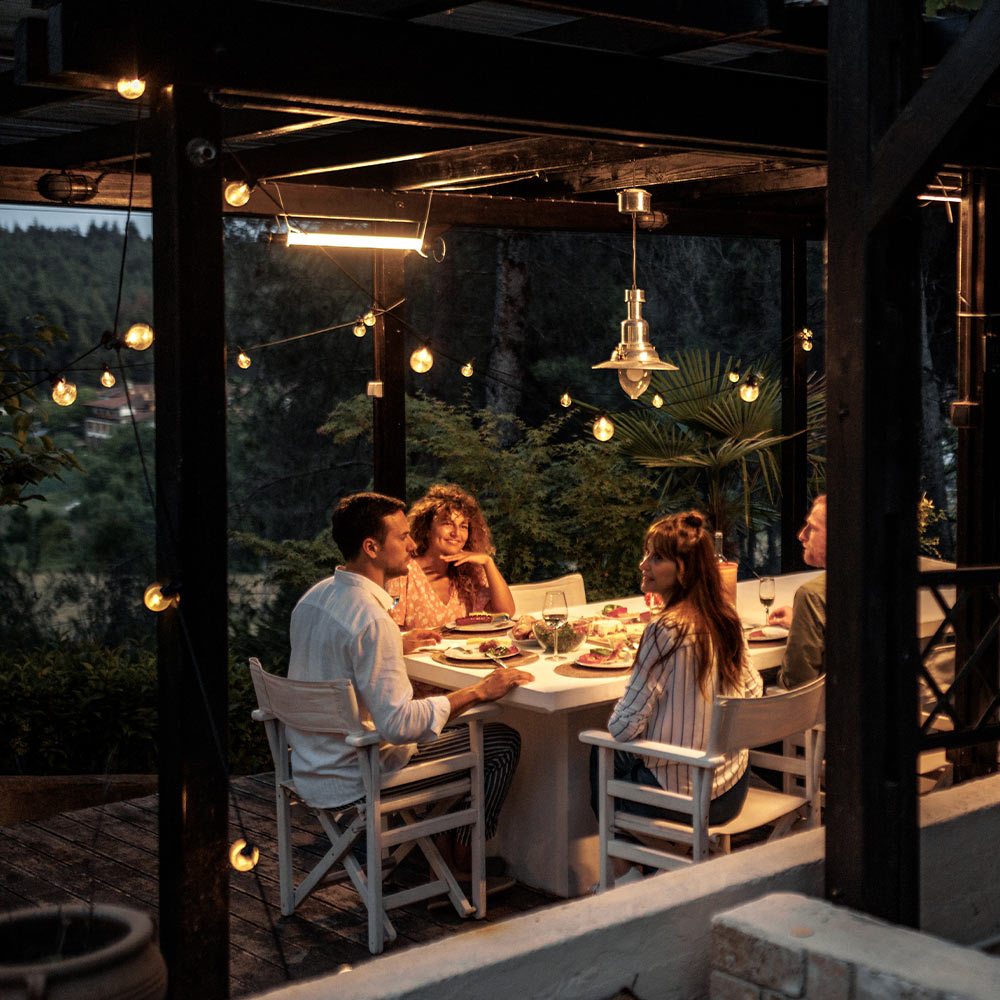 A group of people eating dinner outside with hanging string lights